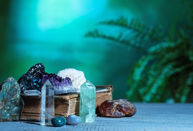 Photo of Beautiful natural gemstones and book on grey table against green background. Space for text