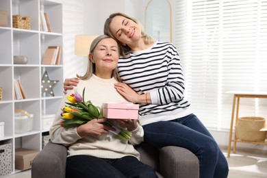 Smiling daughter congratulating her mom with bouquet of tulips and gift at home. Happy Mother's Day