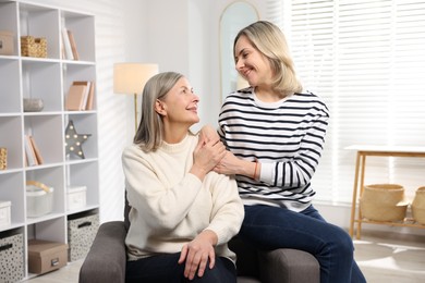 Photo of Smiling daughter and her mother sitting on armchair at home