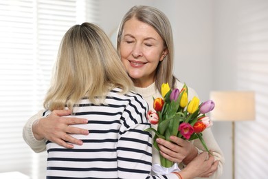 Smiling mom receiving bouquet of tulips from her daughter at home. Happy Mother's Day