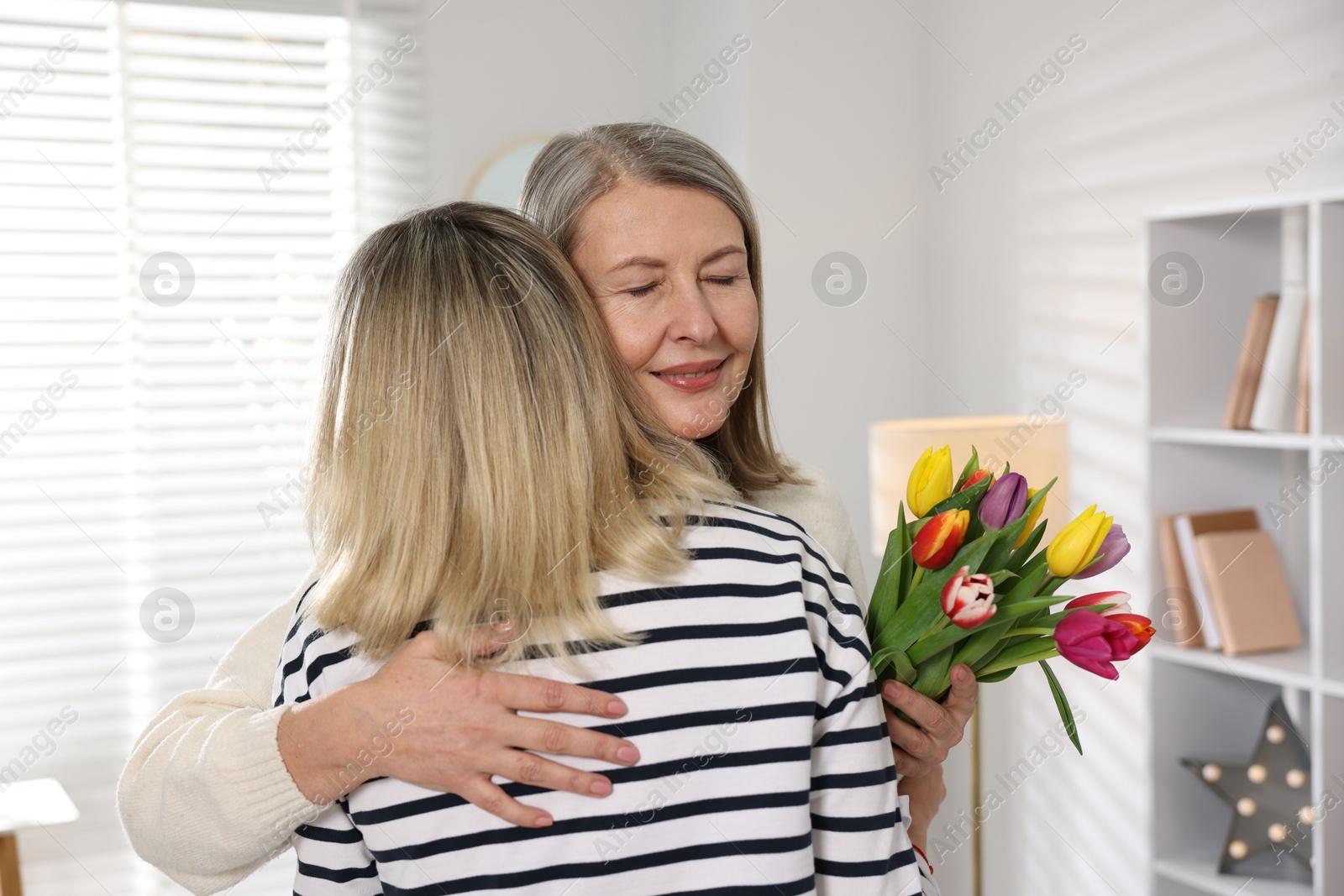 Photo of Smiling mom receiving bouquet of tulips from her daughter at home. Happy Mother's Day