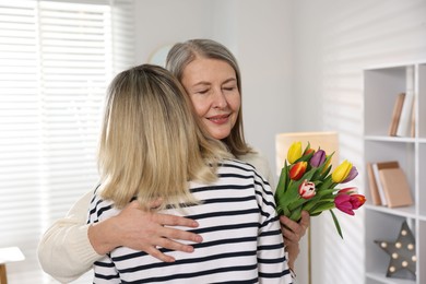 Smiling mom receiving bouquet of tulips from her daughter at home. Happy Mother's Day