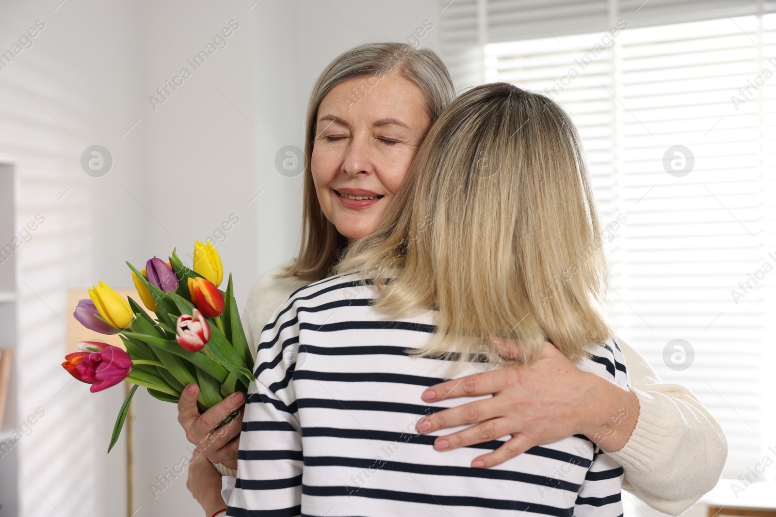 Photo of Smiling mom receiving bouquet of tulips from her daughter at home. Happy Mother's Day