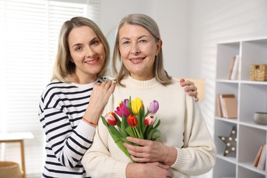 Family portrait of smiling woman with bouquet of tulips and her daughter at home. Happy Mother's Day