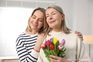 Photo of Woman with bouquet of tulips and her daughter at home. Happy Mother's Day