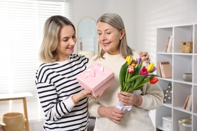 Smiling daughter congratulating her mom with bouquet of tulips and gift at home. Happy Mother's Day