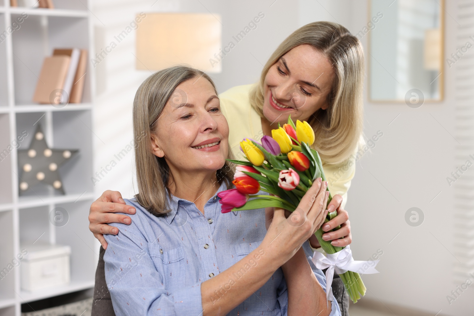 Photo of Smiling daughter congratulating her mom with bouquet of tulips at home. Happy Mother's Day