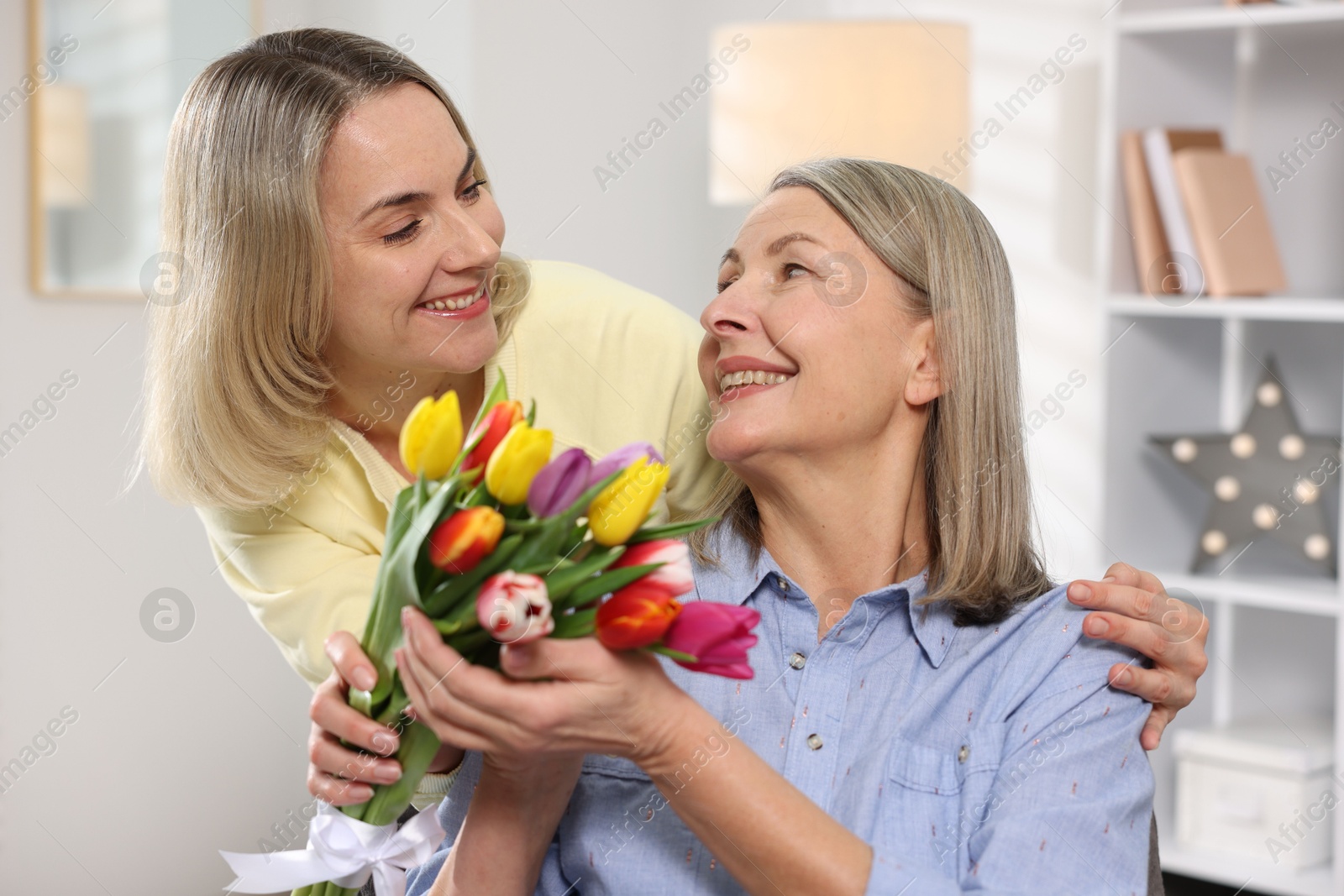 Photo of Smiling daughter congratulating her mom with bouquet of tulips at home. Happy Mother's Day