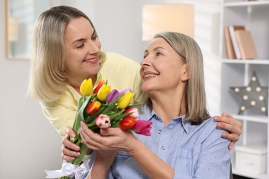 Smiling daughter congratulating her mom with bouquet of tulips at home. Happy Mother's Day