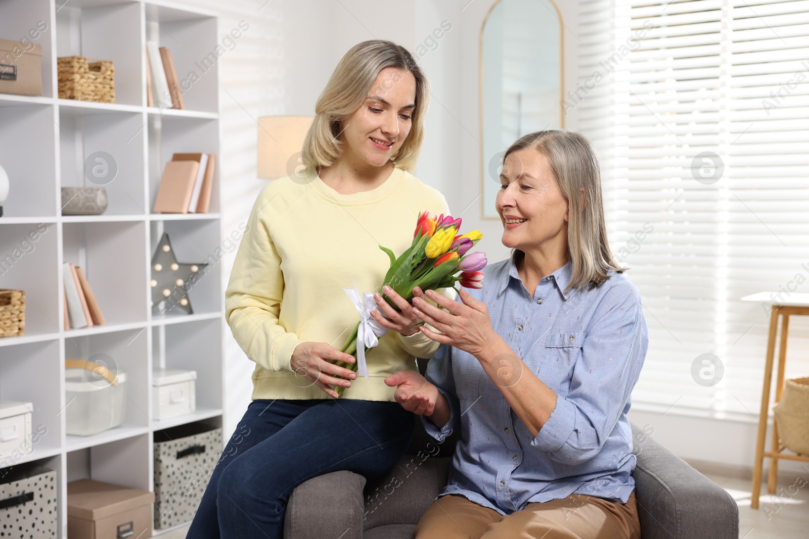 Photo of Smiling daughter congratulating her mom with bouquet of tulips at home. Happy Mother's Day