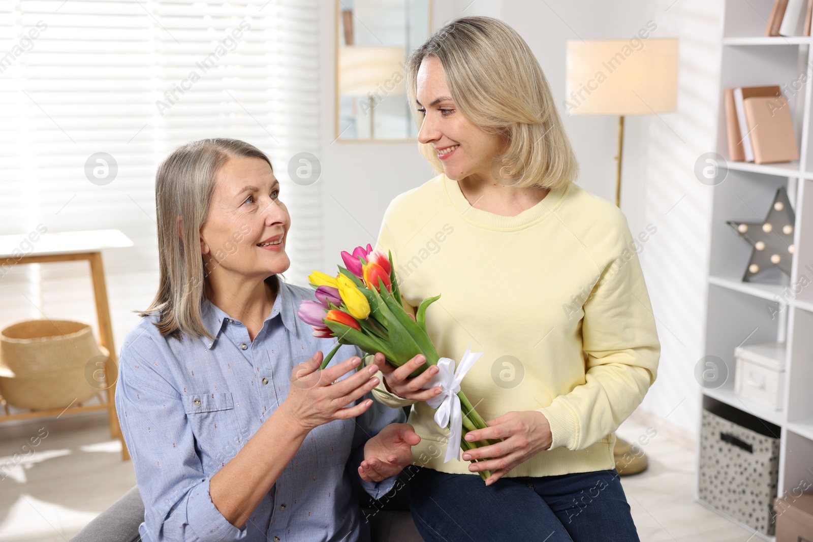 Photo of Smiling daughter congratulating her mom with bouquet of tulips at home. Happy Mother's Day