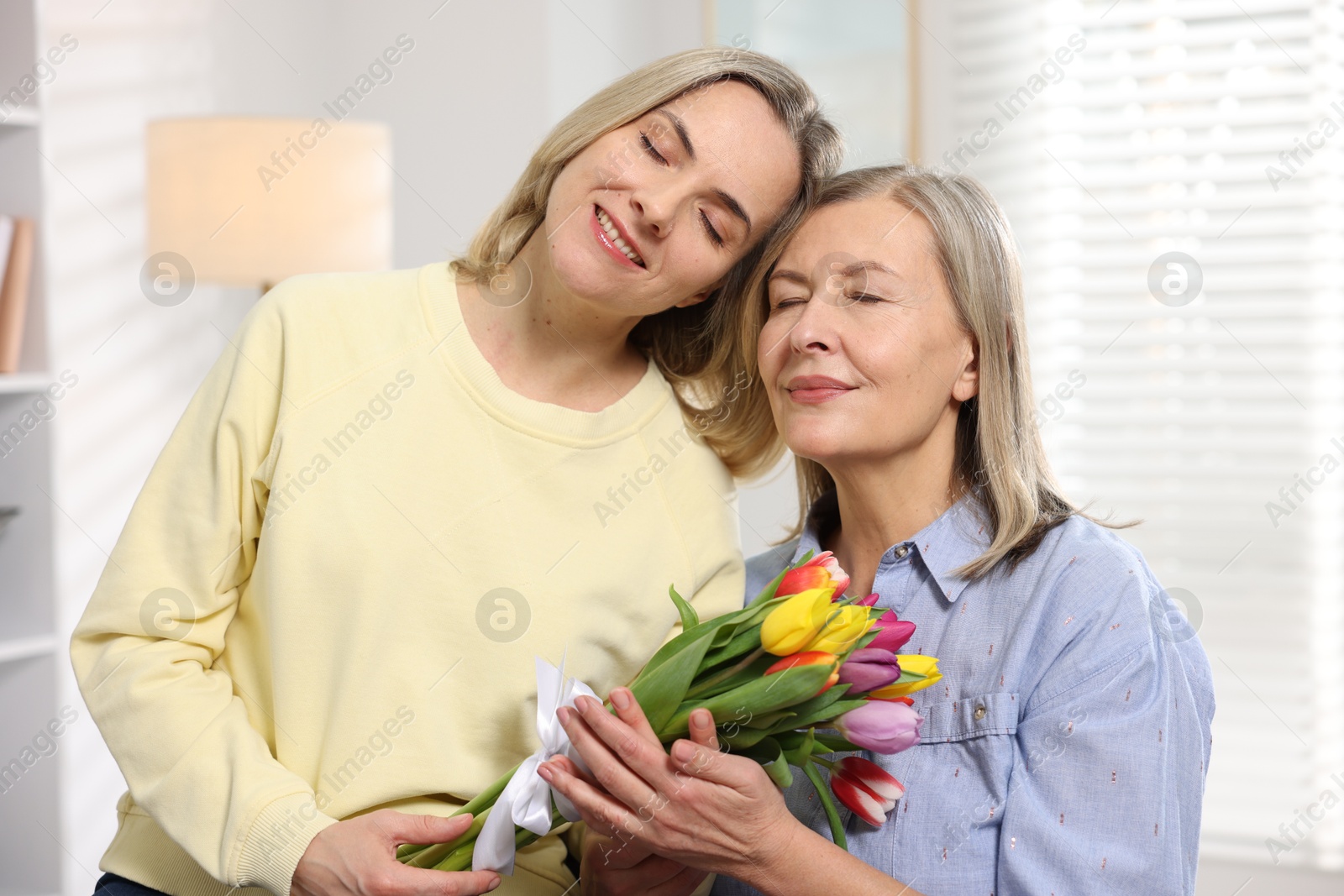 Photo of Smiling daughter congratulating her mom with bouquet of tulips at home. Happy Mother's Day