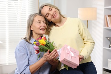 Smiling daughter congratulating her mom with bouquet of tulips and gift at home. Happy Mother's Day