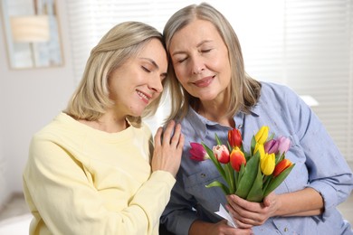 Smiling daughter congratulating her mom with bouquet of tulips at home. Happy Mother's Day