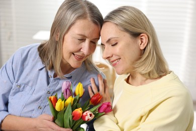 Smiling daughter congratulating her mom with bouquet of tulips at home. Happy Mother's Day