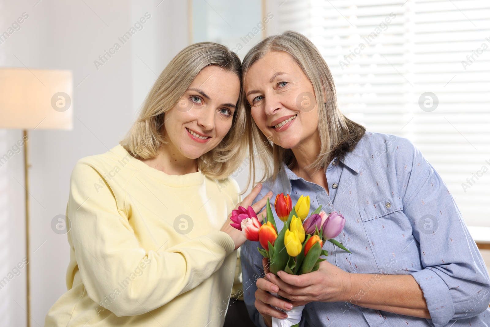 Photo of Smiling daughter congratulating her mom with bouquet of tulips at home. Happy Mother's Day