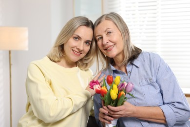 Photo of Smiling daughter congratulating her mom with bouquet of tulips at home. Happy Mother's Day