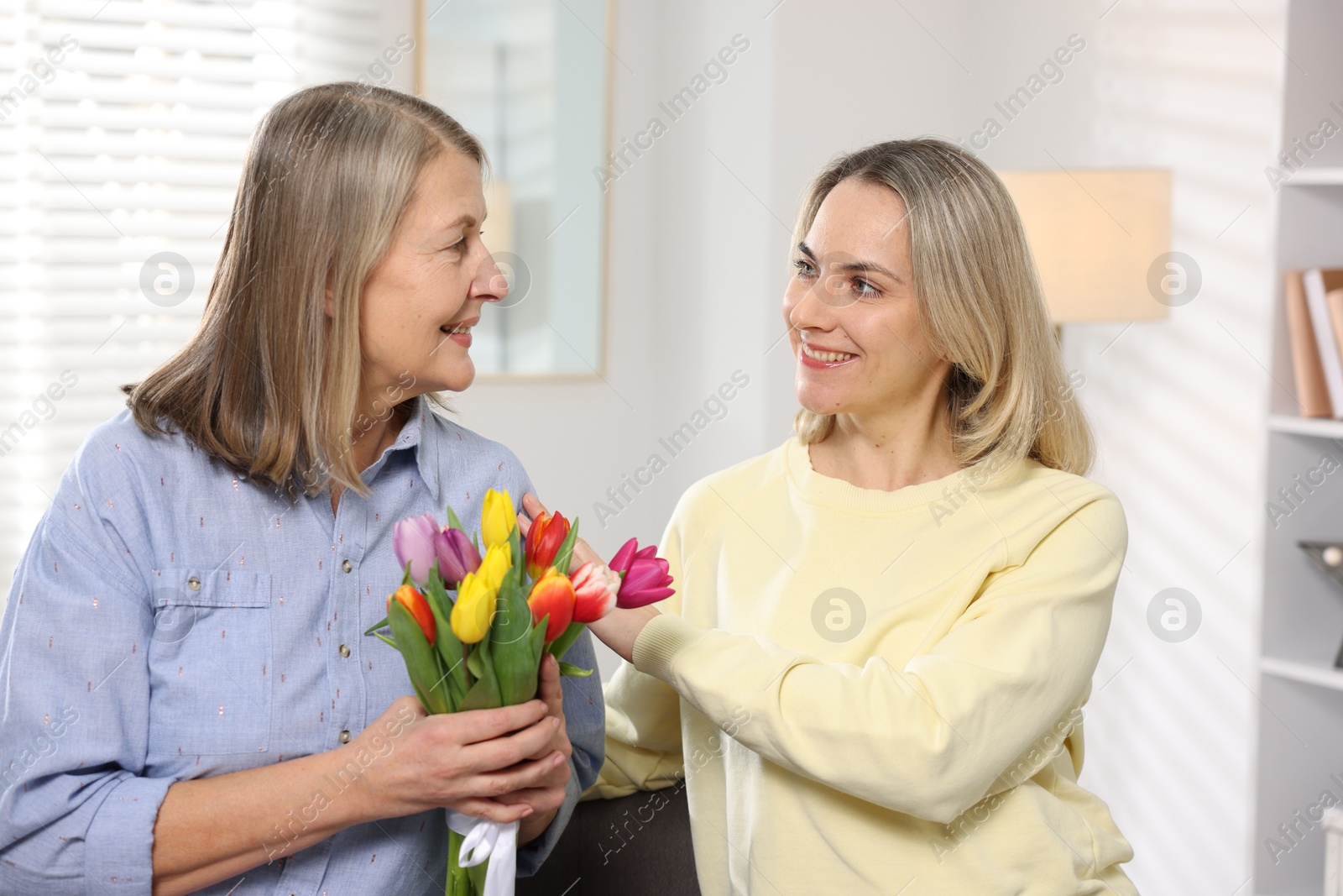 Photo of Smiling daughter congratulating her mom with bouquet of tulips at home. Happy Mother's Day