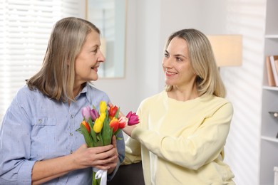 Smiling daughter congratulating her mom with bouquet of tulips at home. Happy Mother's Day