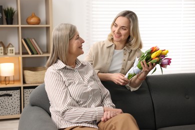 Smiling daughter congratulating her mom with bouquet of tulips at home. Happy Mother's Day