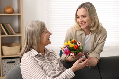 Photo of Smiling daughter congratulating her mom with bouquet of tulips at home. Happy Mother's Day