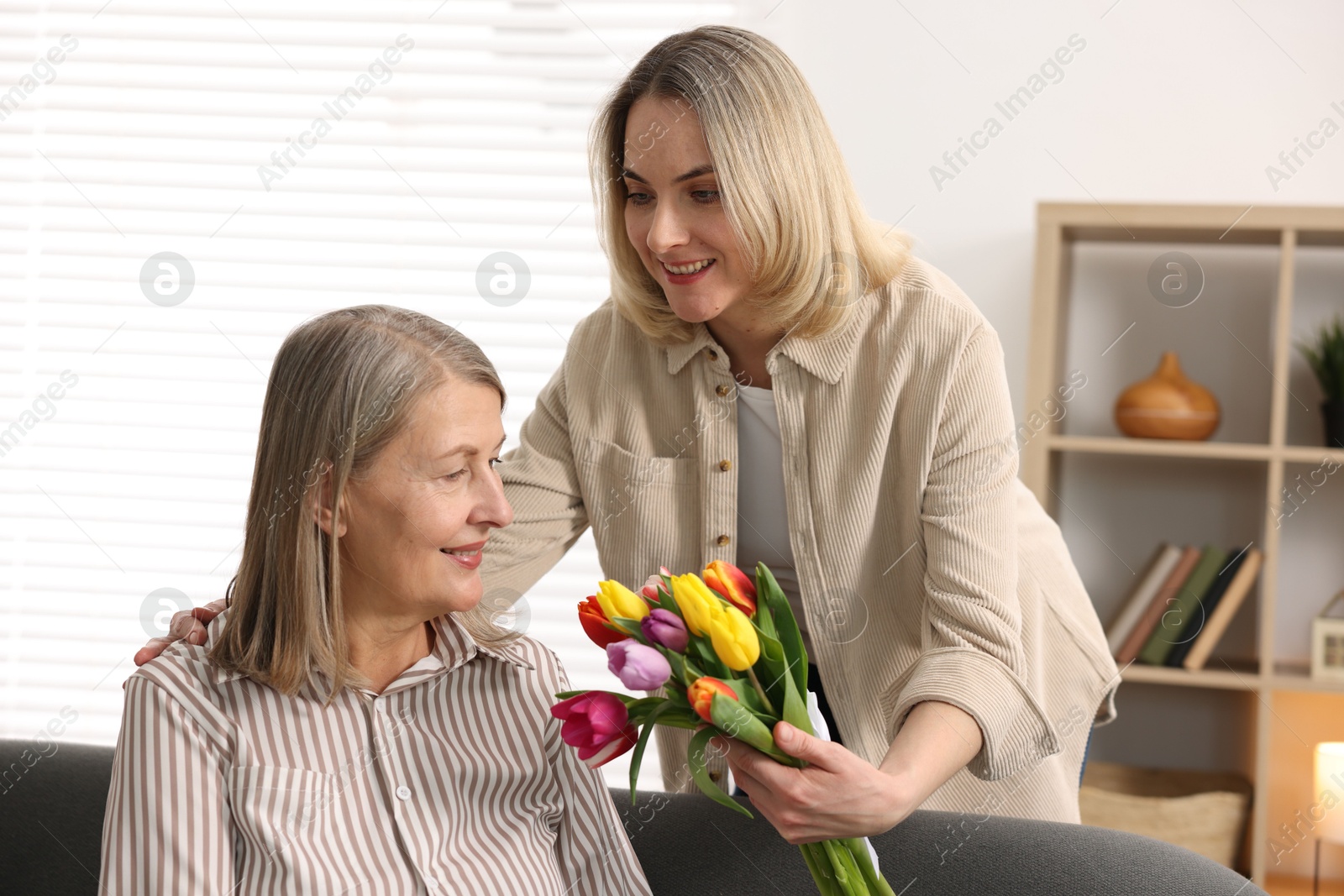 Photo of Smiling daughter congratulating her mom with bouquet of tulips at home. Happy Mother's Day