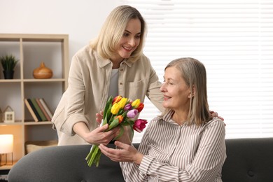 Photo of Smiling daughter congratulating her mom with bouquet of tulips at home. Happy Mother's Day