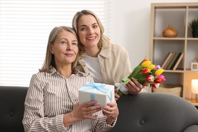 Smiling daughter congratulating her mom with bouquet of tulips and gift at home. Happy Mother's Day