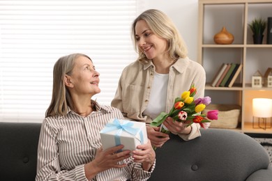 Smiling daughter congratulating her mom with bouquet of tulips and gift at home. Happy Mother's Day