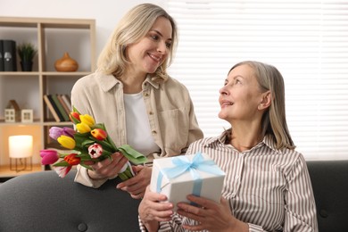 Smiling daughter congratulating her mom with bouquet of tulips and gift at home. Happy Mother's Day