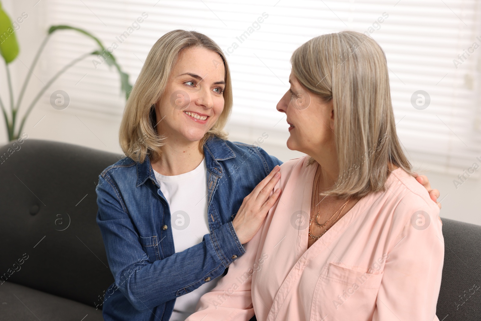 Photo of Smiling daughter and her mother on sofa at home