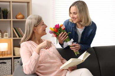 Smiling daughter congratulating her mom with bouquet of tulips at home. Happy Mother's Day