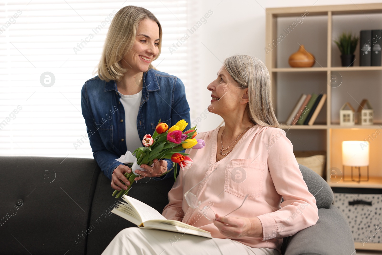 Photo of Smiling daughter congratulating her mom with bouquet of tulips at home. Happy Mother's Day