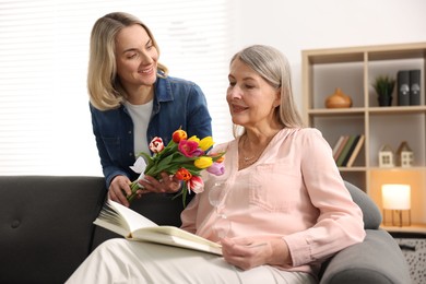 Smiling daughter congratulating her mom with bouquet of tulips at home. Happy Mother's Day