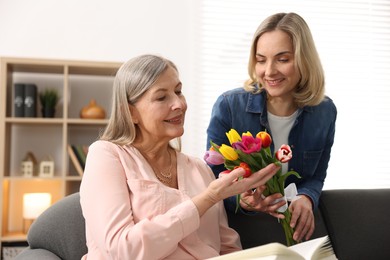 Photo of Smiling daughter congratulating her mom with bouquet of tulips at home. Happy Mother's Day