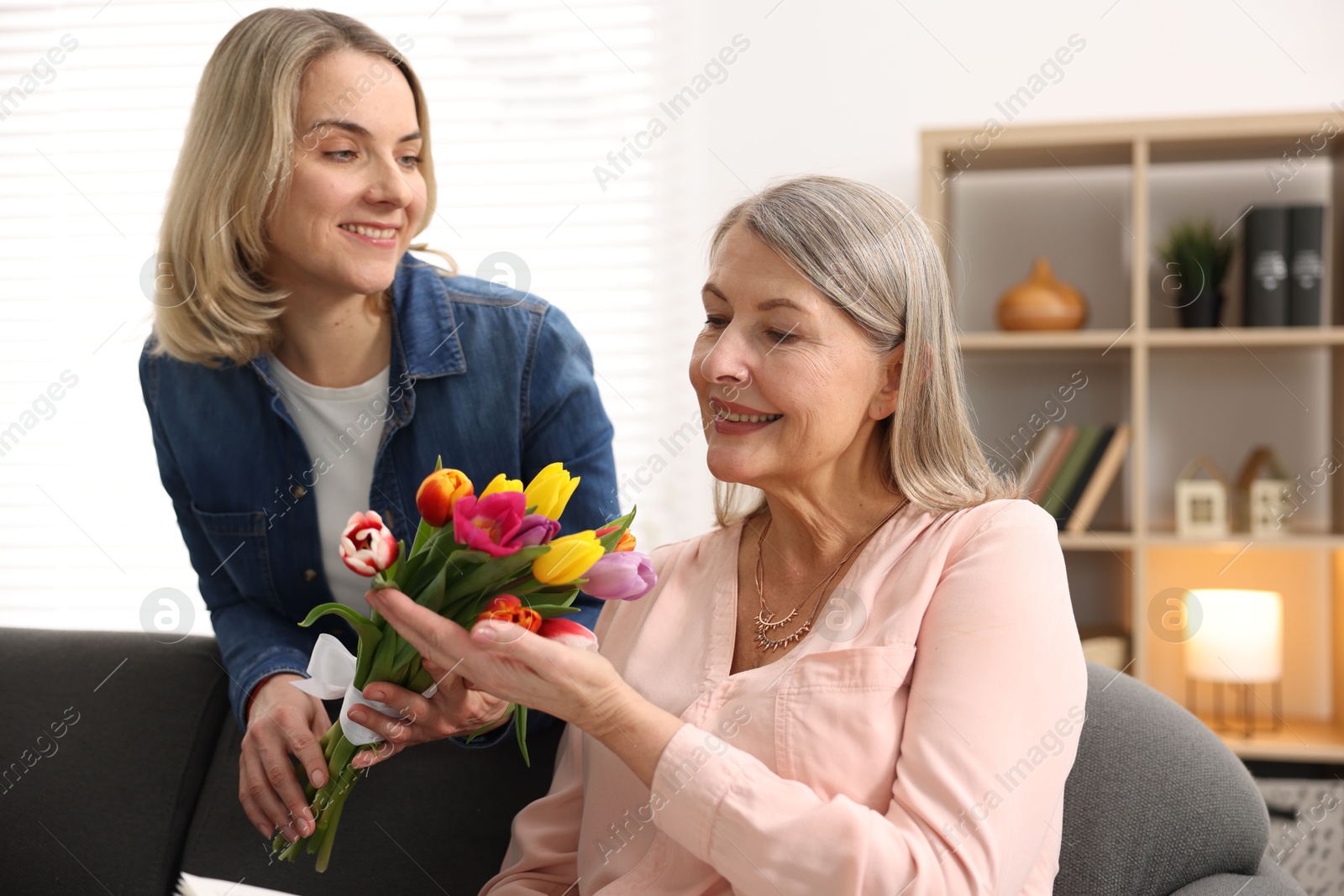 Photo of Smiling daughter congratulating her mom with bouquet of tulips at home. Happy Mother's Day