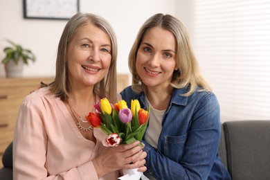 Photo of Smiling woman with bouquet of tulips and her daughter at home. Happy Mother's Day