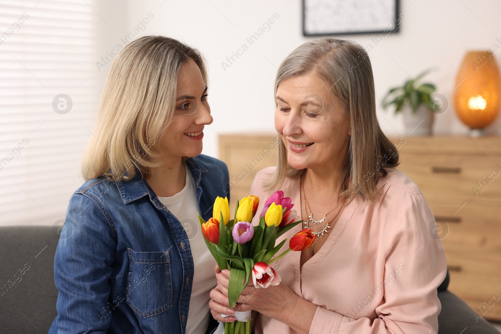 Photo of Smiling woman with bouquet of tulips and her daughter at home. Happy Mother's Day