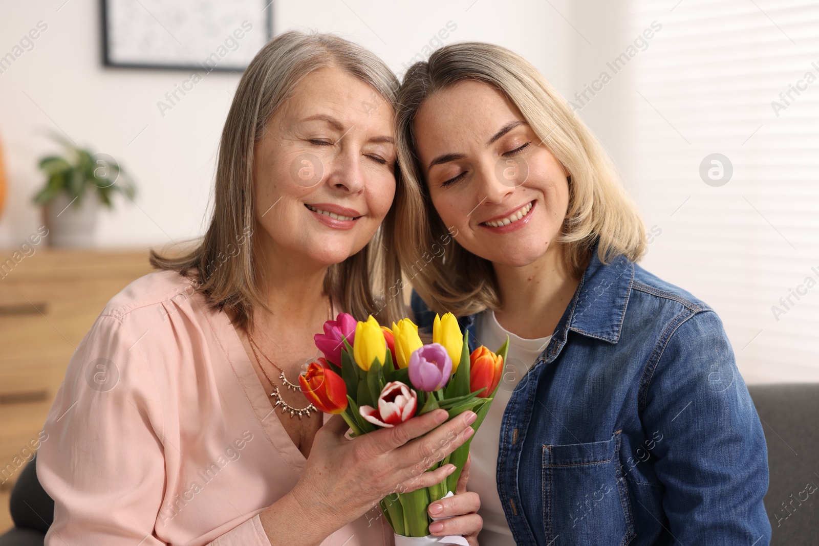 Photo of Smiling woman with bouquet of tulips and her daughter at home. Happy Mother's Day