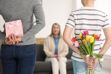 Photo of Mother and son hiding gifts behind backs for their parent at home, selective focus. Happy Mother's Day