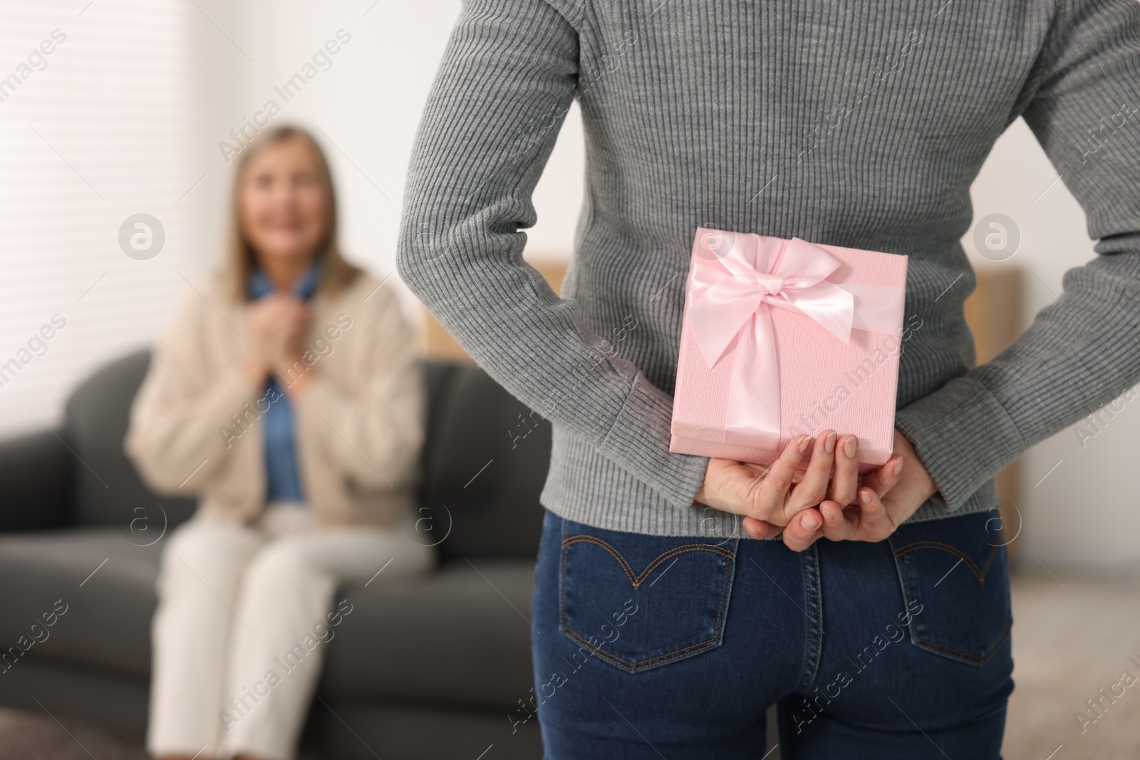 Photo of Daughter hiding gift box behind back for her mom at home, selective focus. Happy Mother's Day