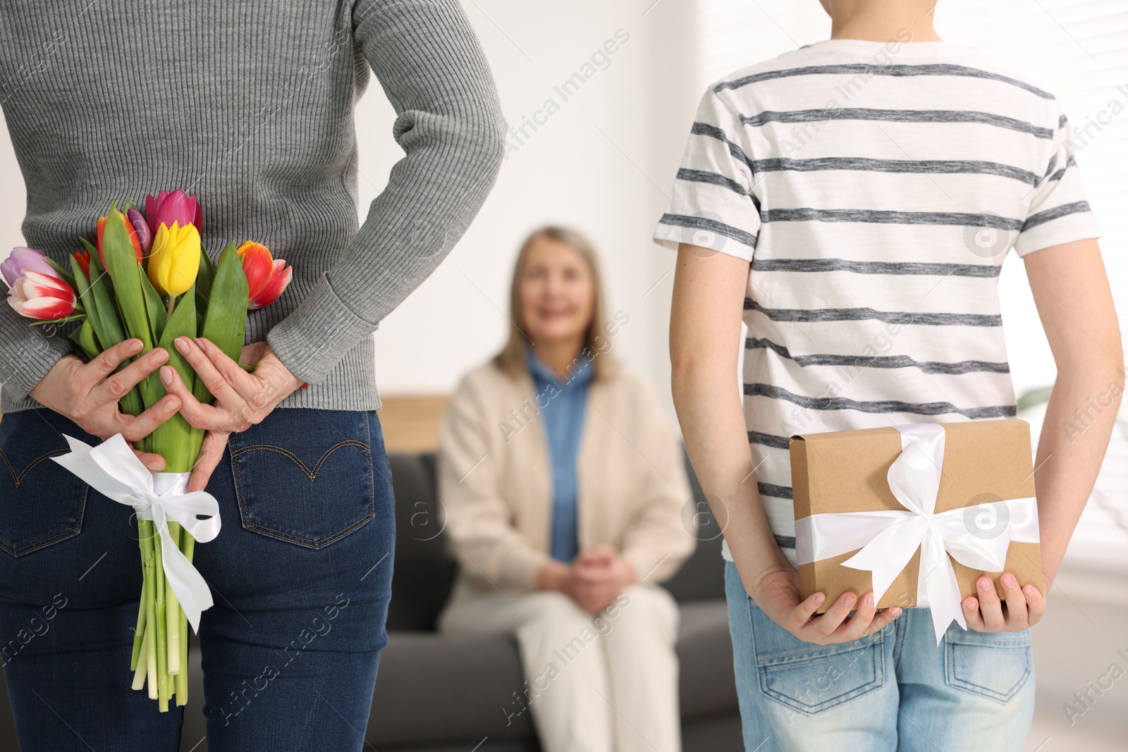 Photo of Mother and son hiding gifts behind backs for their parent at home, selective focus. Happy Mother's Day