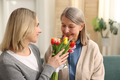 Photo of Smiling daughter congratulating her mom with bouquet of tulips at home. Happy Mother's Day