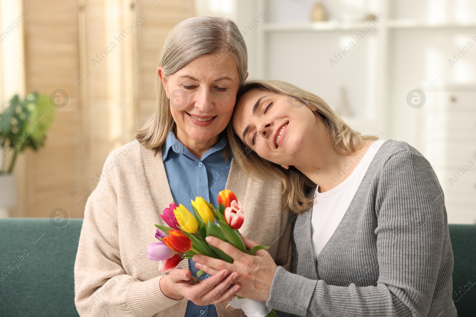 Photo of Smiling woman with bouquet of tulips and her daughter on sofa at home. Happy Mother's Day