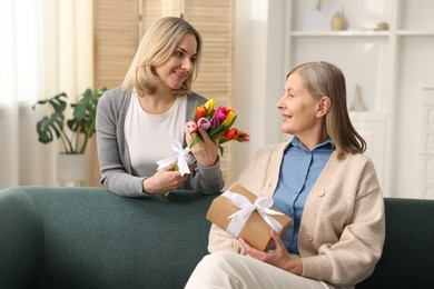 Smiling daughter congratulating her mom with bouquet of tulips and gift at home. Happy Mother's Day