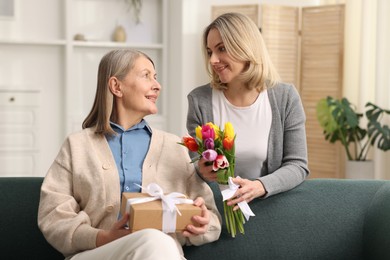 Smiling daughter congratulating her mom with bouquet of tulips and gift at home. Happy Mother's Day