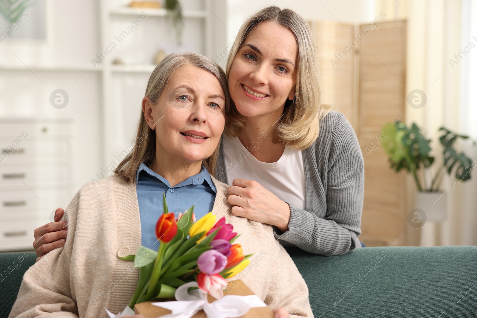 Photo of Family portrait of smiling woman with bouquet of tulips and her daughter at home. Happy Mother's Day