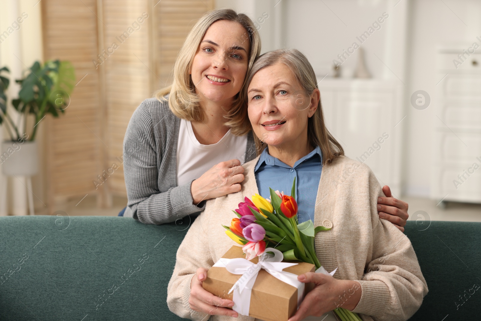 Photo of Family portrait of smiling woman with bouquet of tulips and her daughter at home. Happy Mother's Day