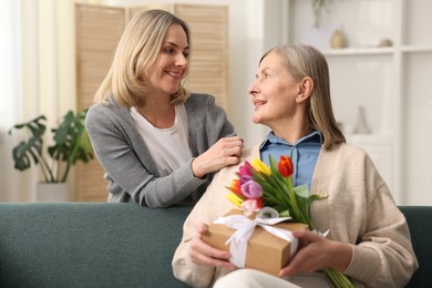 Photo of Smiling woman with bouquet of tulips, gift and her daughter at home. Happy Mother's Day