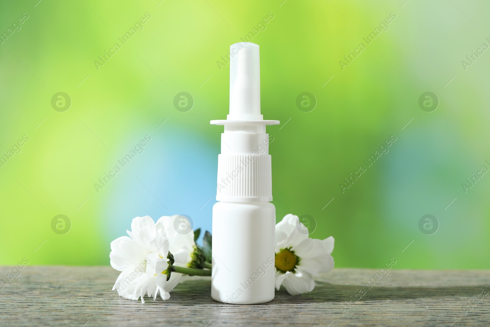 Photo of Allergy treatment. Nasal spray and flowers on wooden table against blurred background